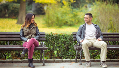 Mann und Frau sitzen auf Parkbank nebeneinander und flirten