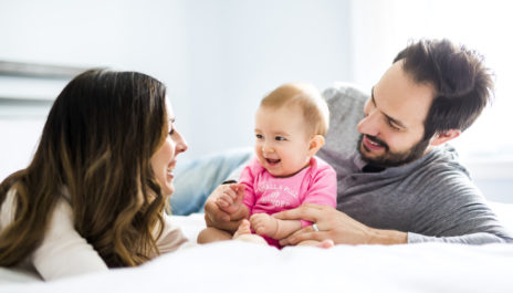 Vater, Mutter und Baby sitzen auf dem Bett